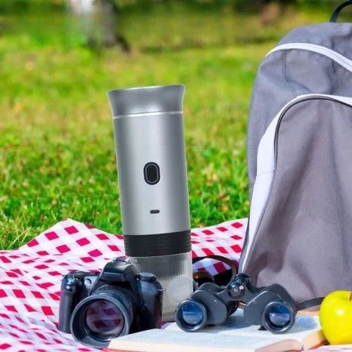 webp, kamp alanında, bahçe alanında, piknikte, kahve makinesi, solunda fotoğraf makinesi, sapında dürbün ve çanta, yer örtüsü üzerinde duruyor,
